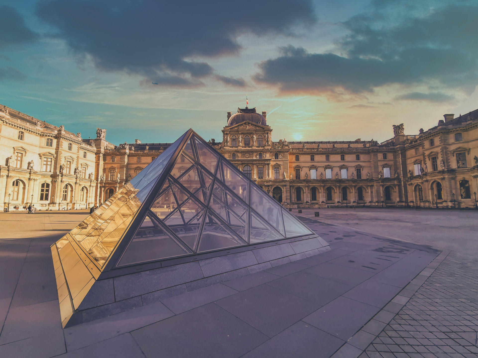 The glass pyramid in the Louvre courtyard at sunset, with the palace and its domed pavilion behind