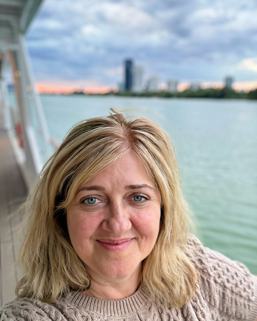 Melinda Muresan on the deck of a river cruise ship, a wide river and city skyline behind her