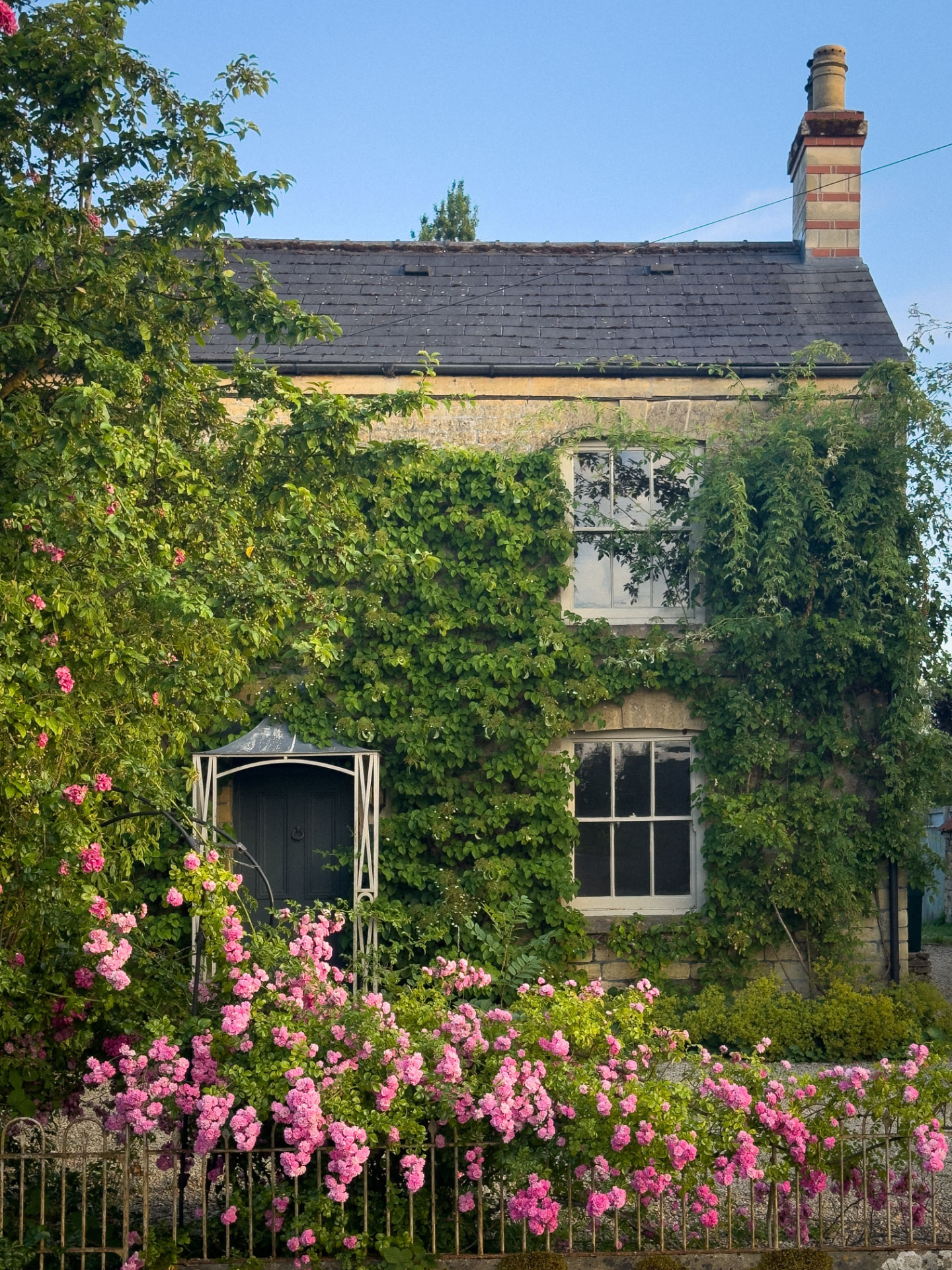 A rose-covered honey-stone cottage in a Cotswolds village, England