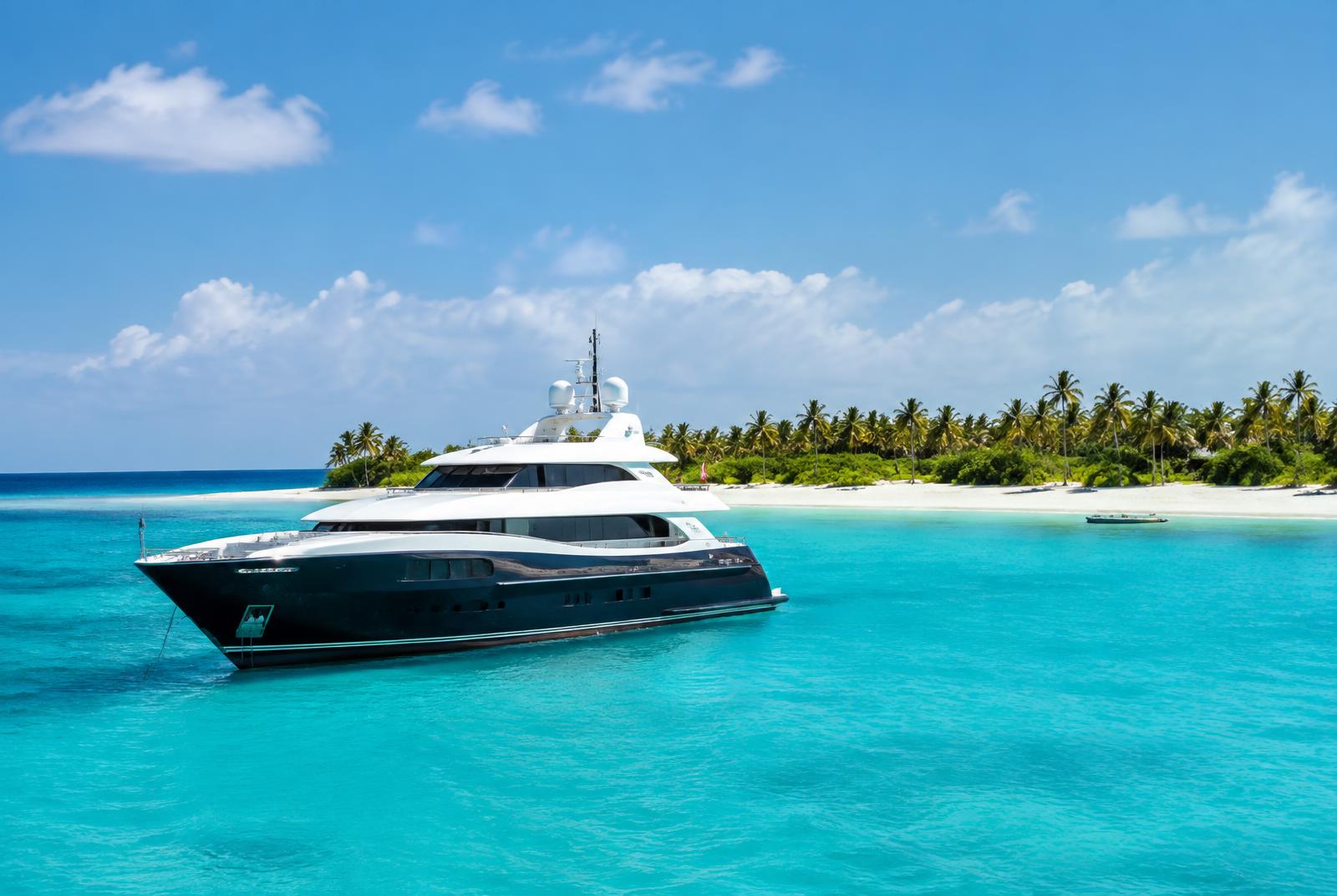 Caribbean yacht charter: a luxury yacht anchored in turquoise water off a white-sand beach lined with palms